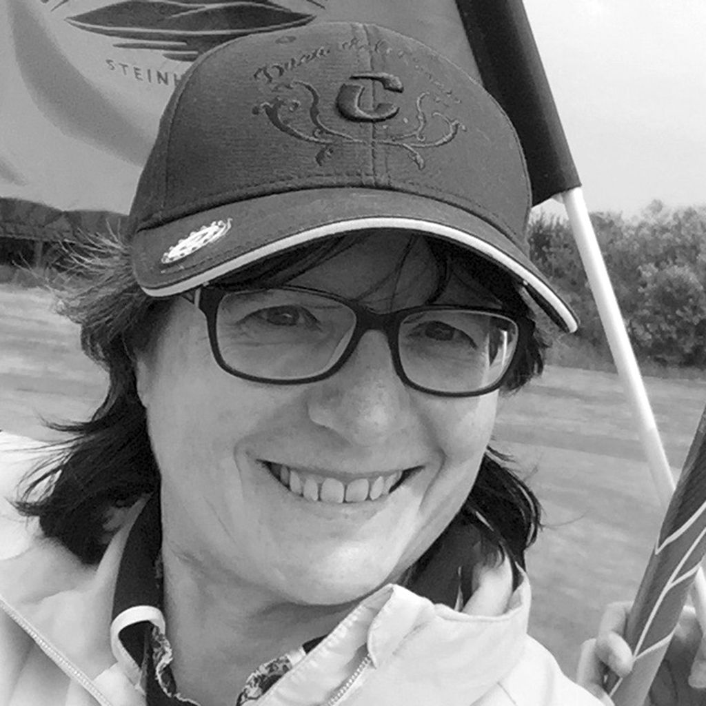 Lächelnde Person mit Cap und Brille hält Fahne, Schwarz-Weiß-Foto.